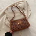 Brown leopard print shoulder bag with a gold bow accent on a cream blazer background - Caramel color
