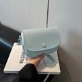 Elegante bolso bandolera azul claro con diseño de lichi y hebilla redonda visto de mano - Azul