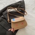 Minimalistische khakifarbene Umhängetasche mit Hasen-Patch auf dunkelgrauem Anzug und Buch - Khaki
