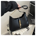 Close-up of black leather underarm bag with gold chain strap on a white suitcase - Black