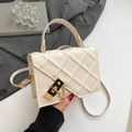Elegant beige quilted crossbody bag with gold chain and metal lock on a textured backdrop - White