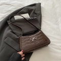 Dunkelbraune Kroko-Schultertasche mit silberner Schleife auf grauem Blazer-Hintergrund - Braun