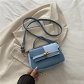 Borsa a sella chic blu bicolore con chiusura a scatto dorata su sfondo blazer bianco - Blu