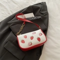 White shoulder bag with strawberry print and red leather strap on grey blazer background - Red