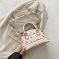 Cream shell crossbody bag with red cherry print and gold hardware on beige blazer - White