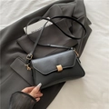 Schwarze minimalistische Schultertasche aus Leder mit goldener Schnalle auf grauem Sakko - Schwarz