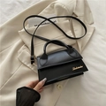 Mini borsa a tracolla nera con logo dorato posata su uno sfondo di blazer beige - Nero
