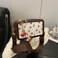 Borsa a tracolla bianca con stampe di ciliegie e finiture in pelle marrone su tavolo - Marrone