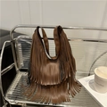 Brown faux leather fringe tote bag with long tassels on a glass shelf in a modern room - Brown