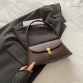 Elegante bolso baguette de cuero marrón oscuro con cierre dorado sobre chaqueta gris - Marrón