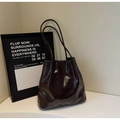Detalle de bolso tote en cuero brillante marrón oscuro con finas correas elegantes - café