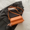 Minimalist orange PU leather flap shoulder bag with gold hardware on a dark grey blazer - Orange