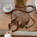 Braune quadratische Ledertasche mit Ringgriff und Gold-Details auf einem Holztisch - Braun