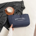 Navy blue nylon tote bag with white lettering and woven handles on black leather backdrop - Blue