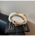 Detail of white leather oval bag with gold C-handle and twin chain straps on art books - White