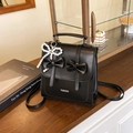 Chic black leather backpack with bow accents and pearl charm on a vintage wooden desk - Black (With Pearl Bow Pendant)