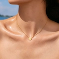 Gros plan d'un collier avec pendentif marguerite dorée porté par un mannequin à la plage - 1 Fleur De Marguerite