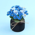 Handgehäkelte blaue Blume im schwarzen Topf mit Blattdetails und dekorativer Schleife - Blumenserie-Verlauf Hellblau Vergissmeinnicht Schreibtisch-Ornament