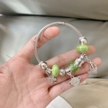 Silver woven beaded bracelet with green charms and clover pendants shown on hand - Green Saturn Open Bracelet