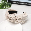 Detail of beige knotted fabric headband with white pearls on a minimalist background - Beige