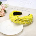 Close-up of bright yellow knotted headband with faux pearls on textured fabric - Yellow