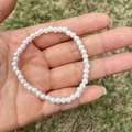 Close-up of a child's white faux pearl bracelet held in a hand over a grassy background - 4MM Cream White Pearl Bracelet