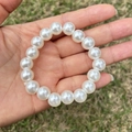 Detailed view of child's white imitation pearl beaded bracelet worn on a girl's wrist - 10MM Cream White Pearl Bracelet