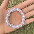 Close-up of a white imitation pearl bracelet for girls held over a green grass background - 10MM Pure White Pearl Bracelet