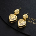 Detalle macro de pendientes de corazón dorados con circonitas y trébol en cuero negro - Dorado