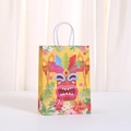 Detail of yellow Tiki party gift bag with tropical mask print and white handles - Kraft Paper / Yellow Tiki Mask (494-5) / 21x15x8cm