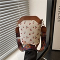 Chic cream canvas bucket bag with cherry print and geometric wide strap on a white background - Brown