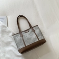 Detail of grey canvas tote with brown leather trim and fashion brand tag on white cloth - Gray