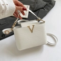 White woven bucket bag with gold V logo held against a dark suit background - White