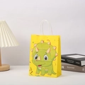 Close-up of yellow kraft paper gift bag with cartoon triceratops and white handles - 21x15x5 / Yellow