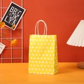 Close-up of a yellow polka dot paper gift bag with white twisted rope handles on a desk - 15x11x6cm / Yellow