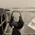Chic black leather crescent handbag with gold hardware displayed on a modern shelf - Black