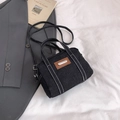 Detail of black denim tote bag with white contrast stitching and metallic logo plate - Black