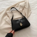 Elegant black shoulder bag with gold gourd-shaped clasp on a beige blazer background - Black