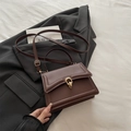 Deep brown structured handbag with gold dual-ring buckle on a charcoal grey blazer - Brown