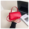 Detalle de un bolso de piel roja con solapa ondulada y asa superior sobre un escritorio - Rojo