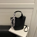 Bolso tipo cubo de cuero negro con pañuelo de lunares sobre un libro minimalista - Negro