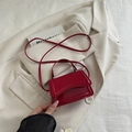 Mini red patent leather handbag with crossbody strap displayed on a beige blazer - Red