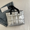 Bolso tote acolchado plateado metalizado con asas negras sobre fondo minimalista - Plateado