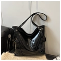 Detail of black glossy faux leather tote bag featuring vertical stitching and silver rivets - Black