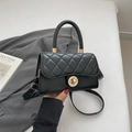 Bolso acolchado negro con cierre dorado sobre fondo de chaqueta elegante - Negro