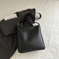 Bolso bucket minimalista de cuero negro con correa ancha sobre tela blanca texturizada - Negro