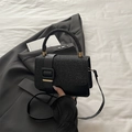 Structured black handbag with sequined trim and square buckle on a grey blazer - Black