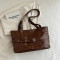 Bolso tote marrón de cuero sintético con hebilla plateada sobre fondo de blazer neutro - Marrón