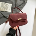 Elegante burgunderrote Umhängetasche mit goldener Schließe vor einem grauen Blazer - Rot
