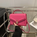 Minimalistische fuchsia Lederhandtasche mit goldenem Oval-Drehverschluss auf Metallregal - Rosenrosa